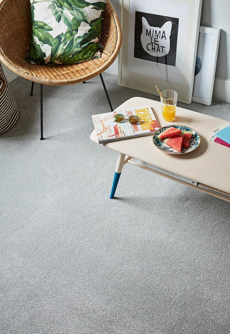 Light grey carpet in a living room with a rattan chair and a low table with books and fruit.