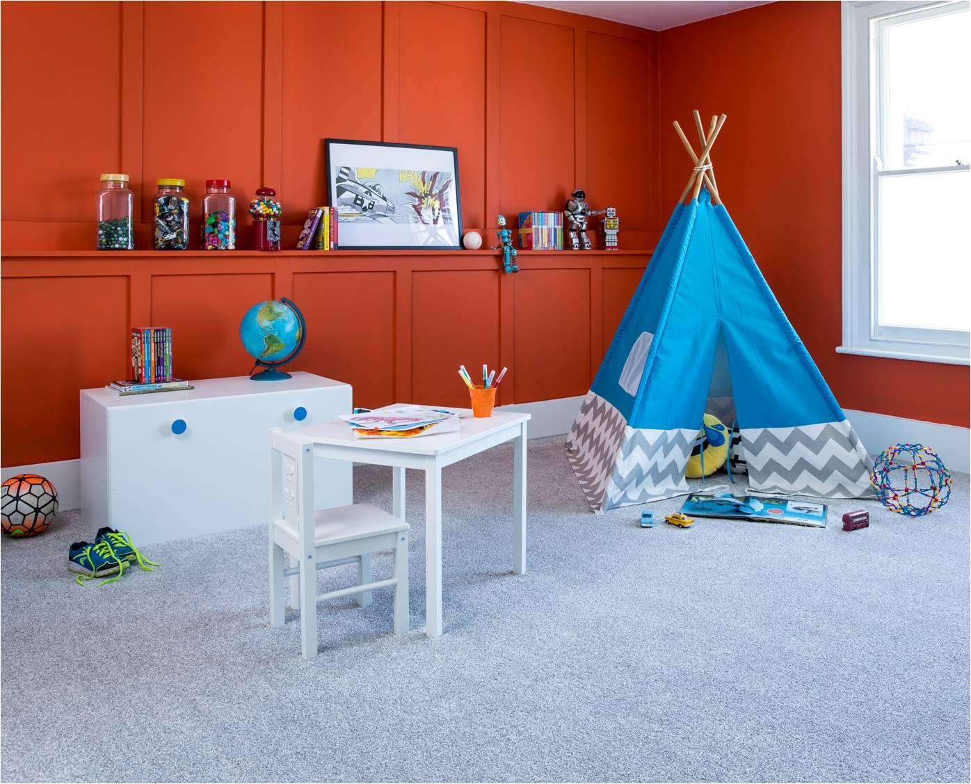 Light grey carpet in modern kids playroom with orange wall, white furniture and blue teepee tent