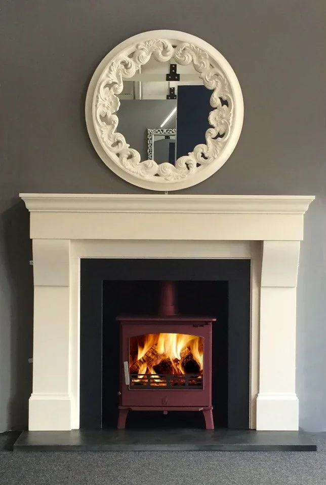 Cabra limestone fireplace with black hearth and red wood-burning stove, ornate mirror above