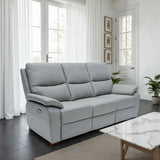 A light gray three-seat reclining sofa in a bright, modern living room with white curtains, dark wood floors, and a marble-top coffee table.