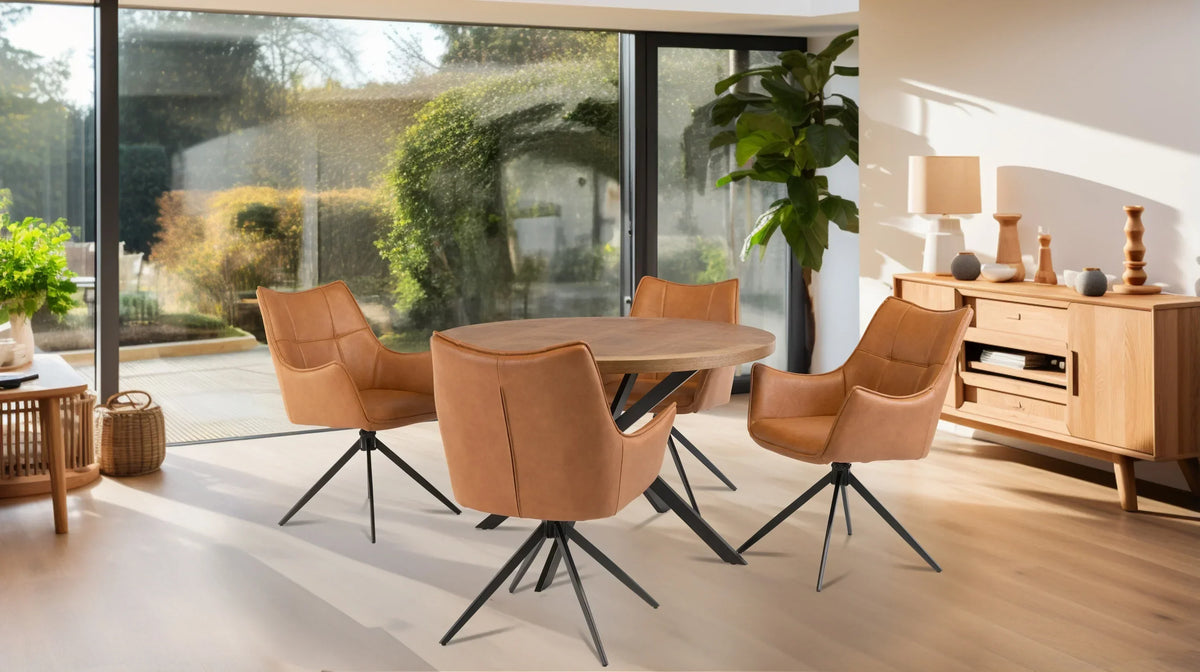 Round oak dining table with four tan leather chairs in modern dining room with large windows