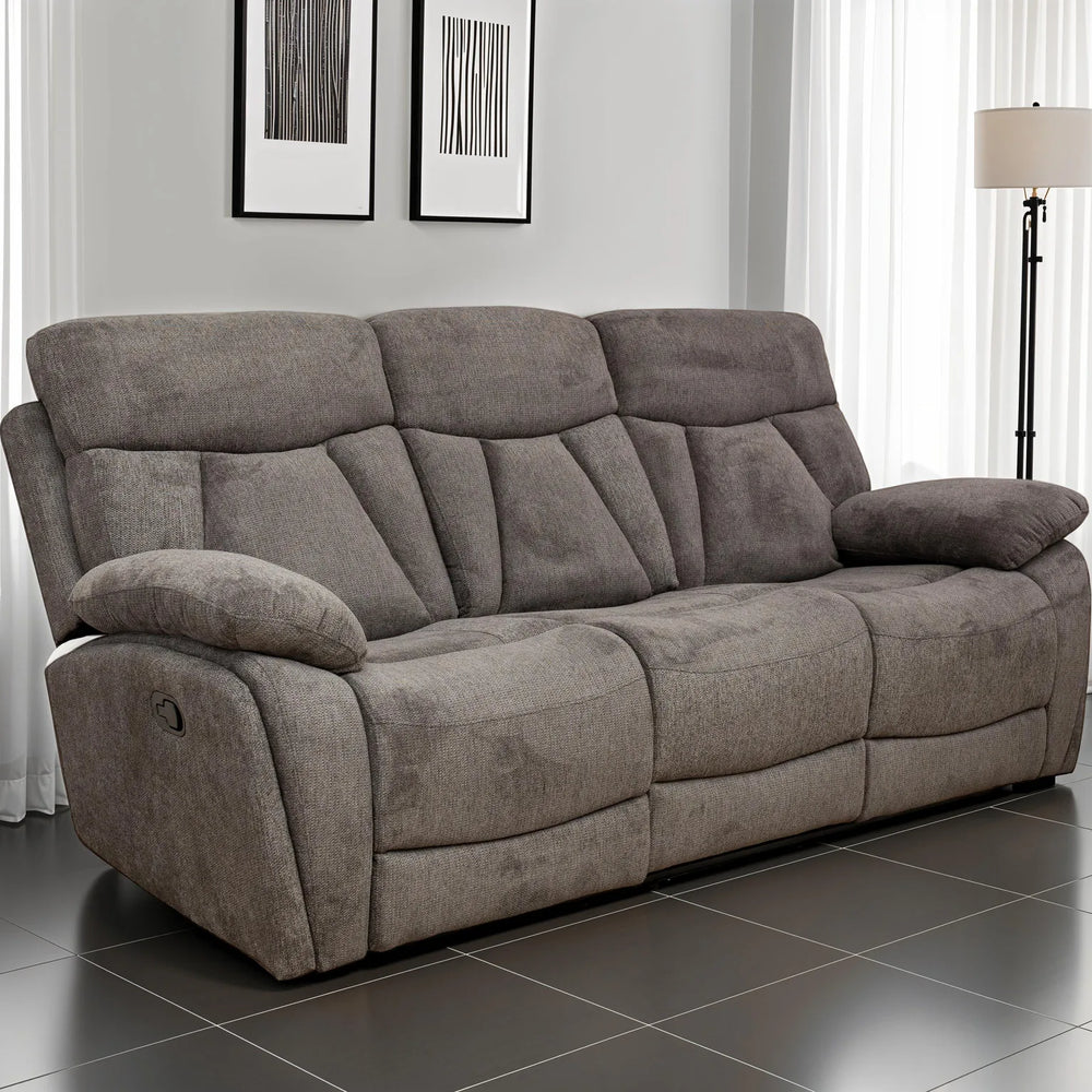 A three-seat gray reclining sofa with plush padded cushions, shown in a modern living room setting with dark tiled flooring, white curtains, and a floor lamp.