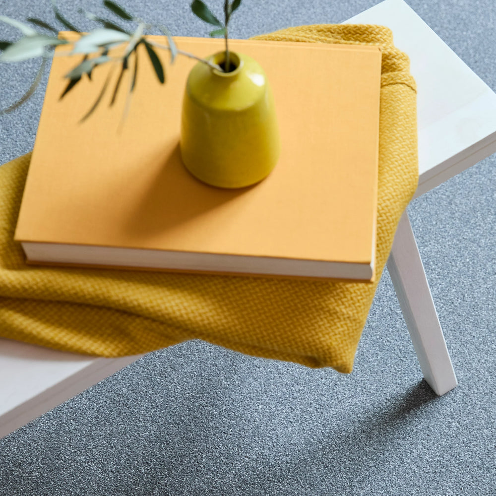Soft grey carpet with a subtle speckled texture under a white table with a yellow book and vase.