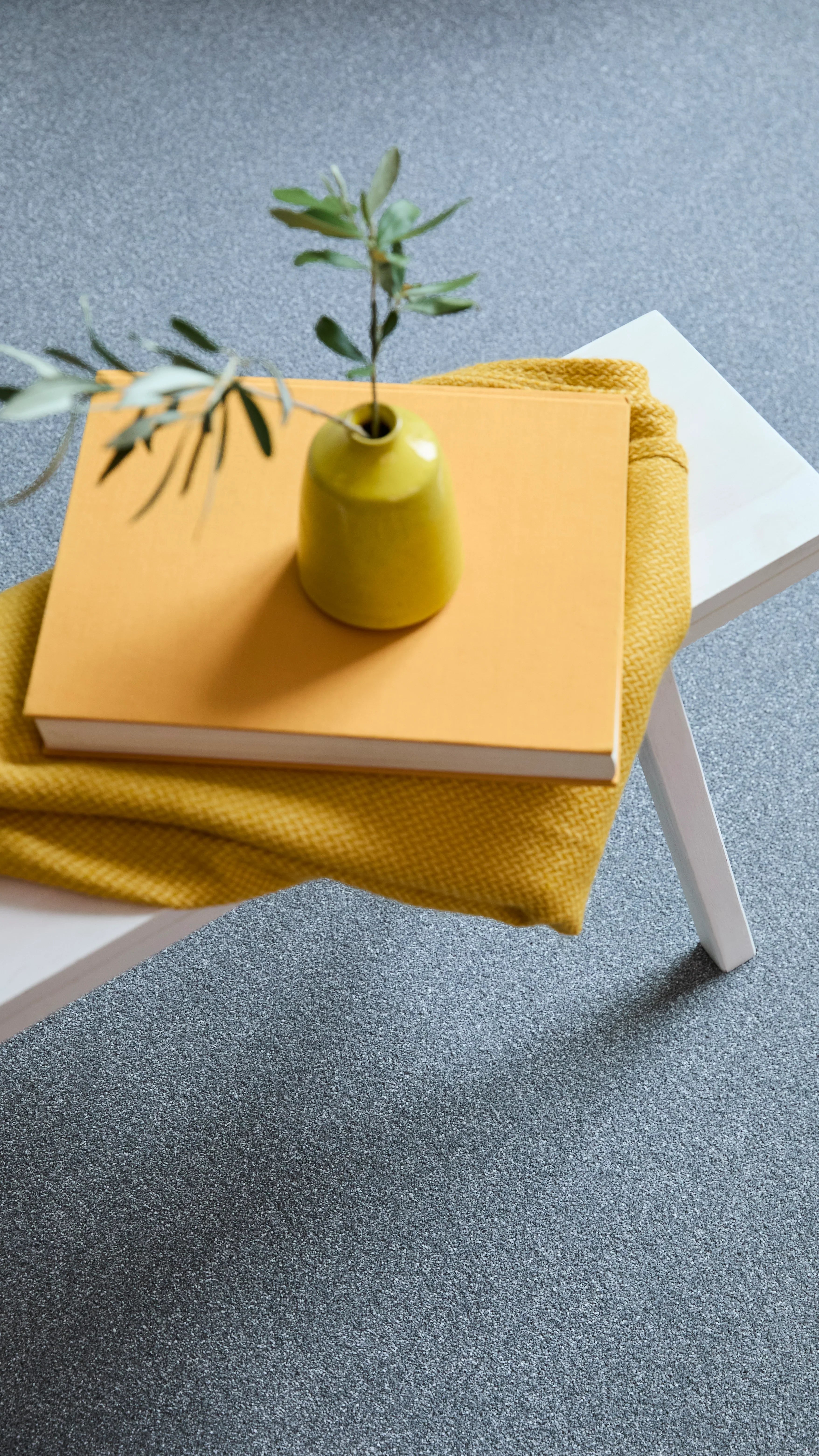 Soft grey carpet with a subtle speckled texture under a white table with a yellow book and vase.