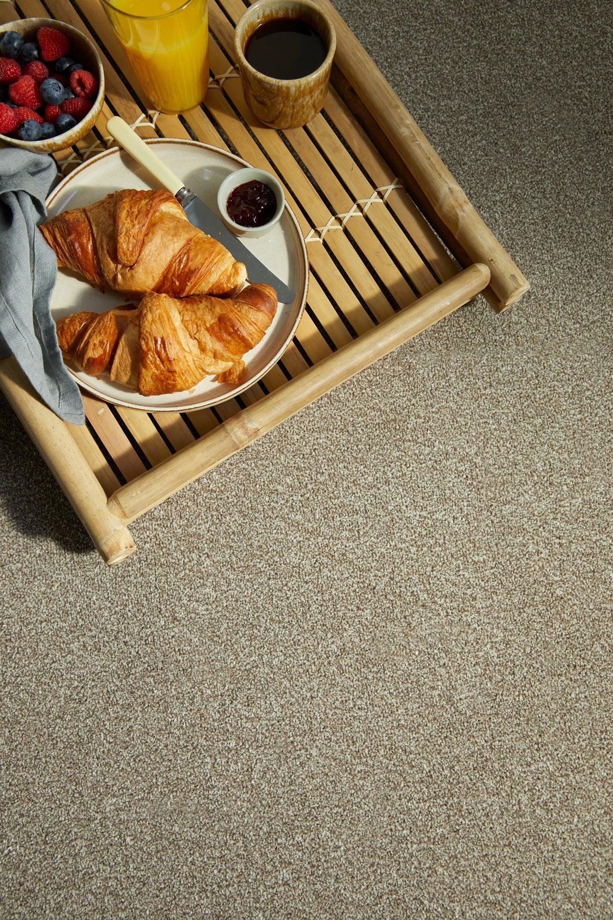 Beige Kingston Kernel carpet with breakfast tray, croissants and drinks on textured surface