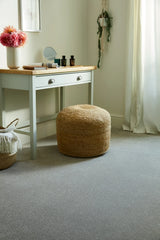 Grey carpet in a bedroom with a woven pouf and light wooden vanity table