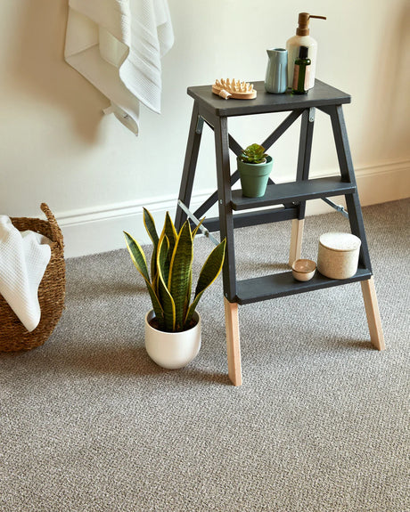 Dark grey step stool with natural wood legs, styled with plants and toiletries in a bathroom.