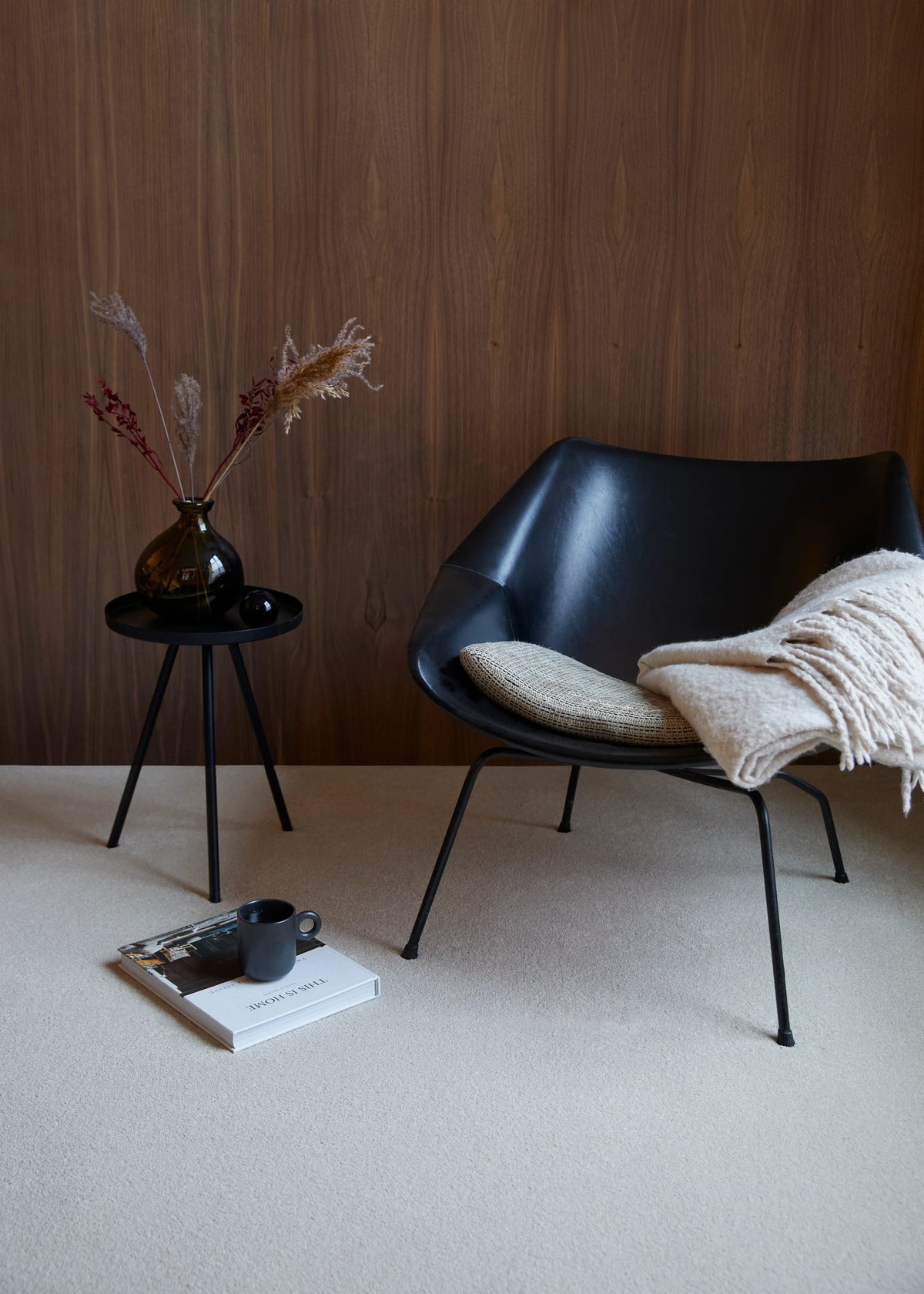 Black modern chair with a beige cushion, styled with a side table and vase on cream carpet
