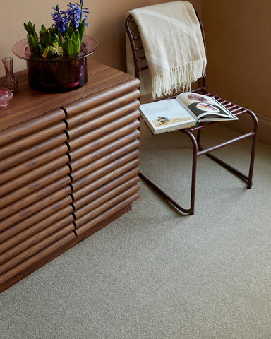 Light beige carpet in a living room with a wooden sideboard and metal chair with a blanket