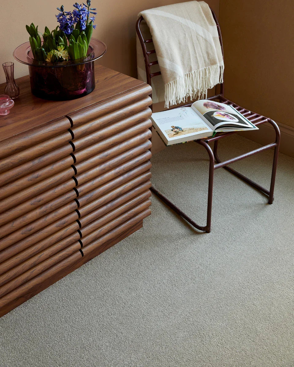 Light beige carpet in a living room with a wooden sideboard and metal chair with a blanket