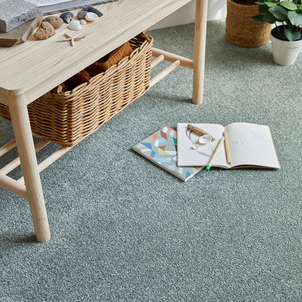 sage green saxony carpet in living room with wooden table, wicker basket, and houseplants