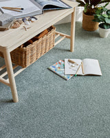 sage green saxony carpet in living room with wooden table, wicker basket, and houseplants