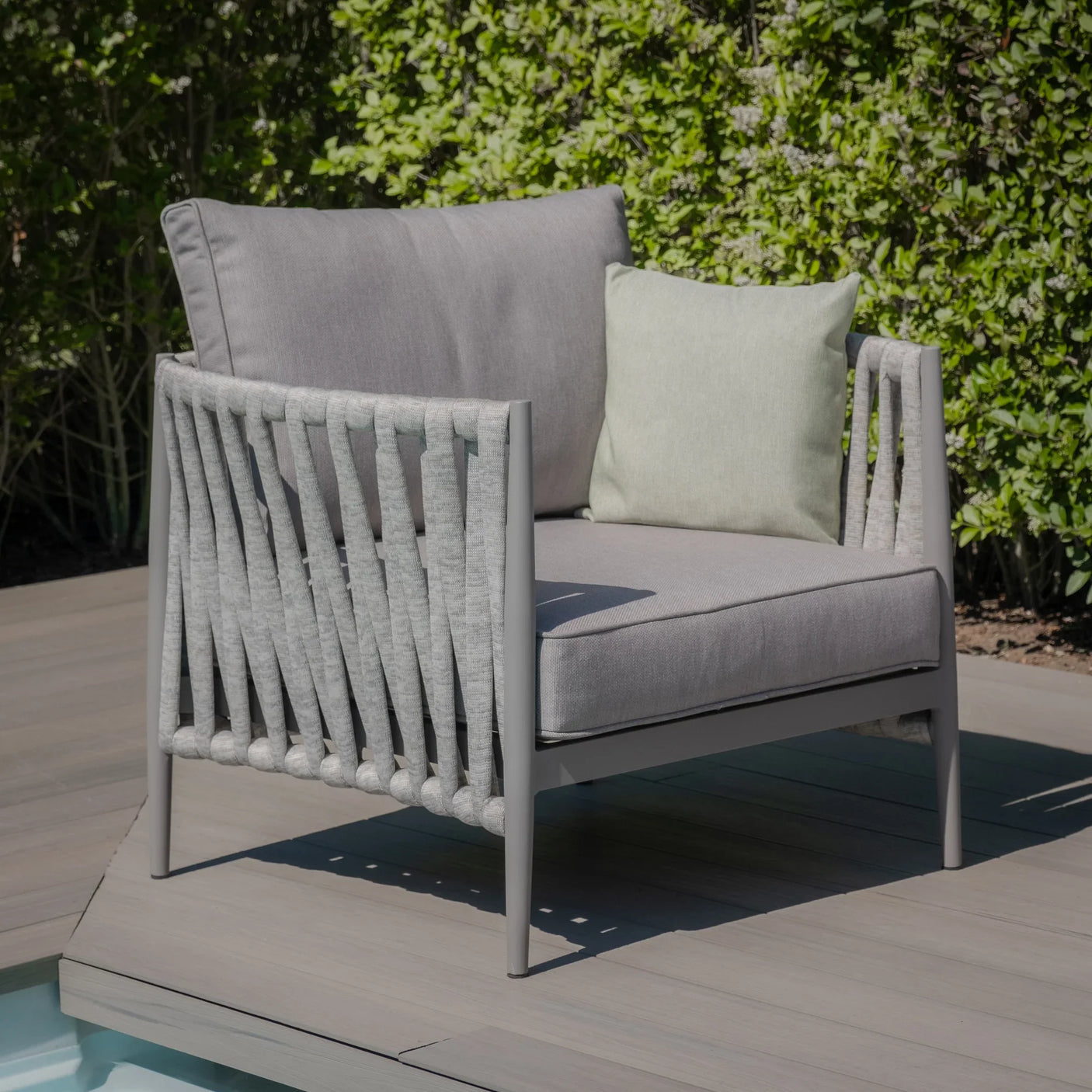Grey outdoor armchair with rope detail and cushions on deck by garden hedge