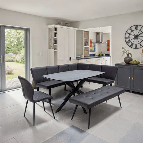 A modern dining set in a bright, contemporary dining room. The set includes a rectangular gray table with black crossed legs, a tufted corner banquette, a matching seat bench, and a gray upholstered chair with black legs.