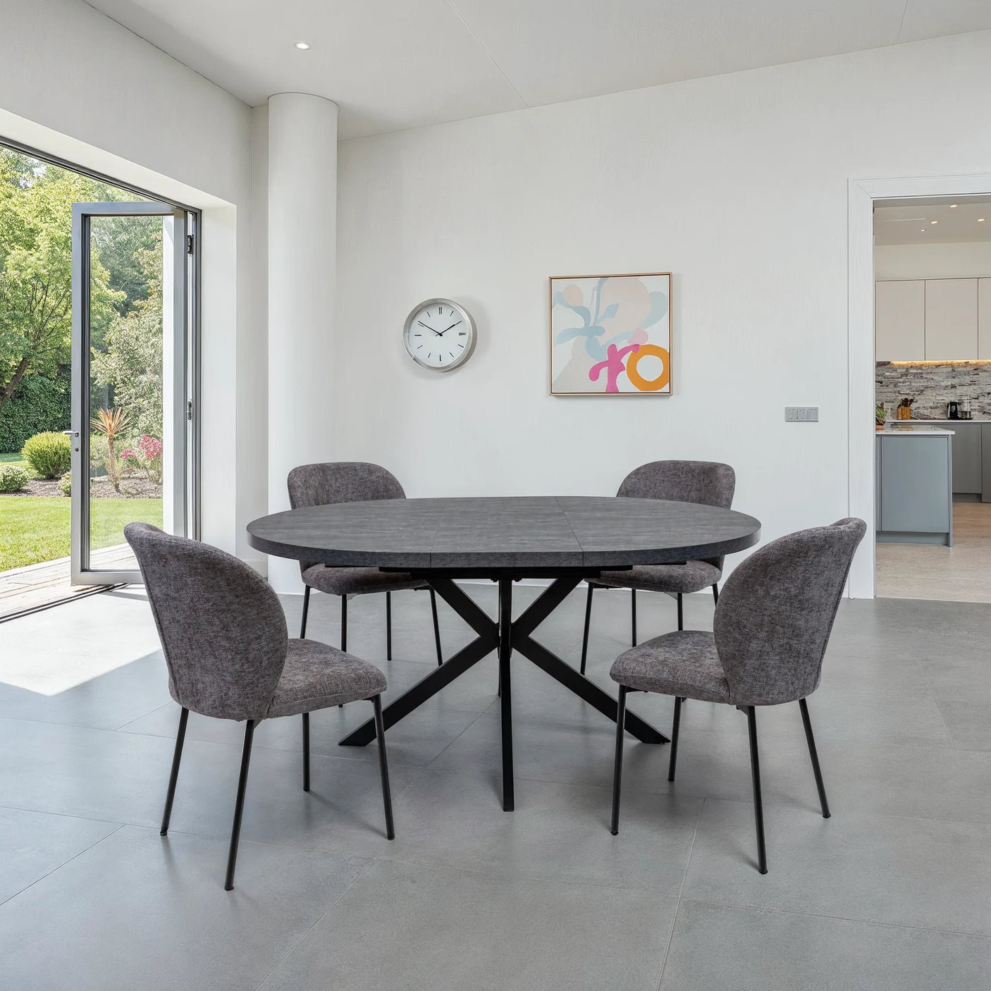 A modern dining set featuring a dark gray oval stone table and four gray upholstered chairs with black metal legs, set in a bright, minimalist dining room.