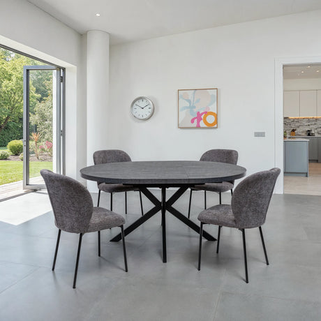A modern dining set featuring a dark gray oval stone table and four gray upholstered chairs with black metal legs, set in a bright, minimalist dining room.