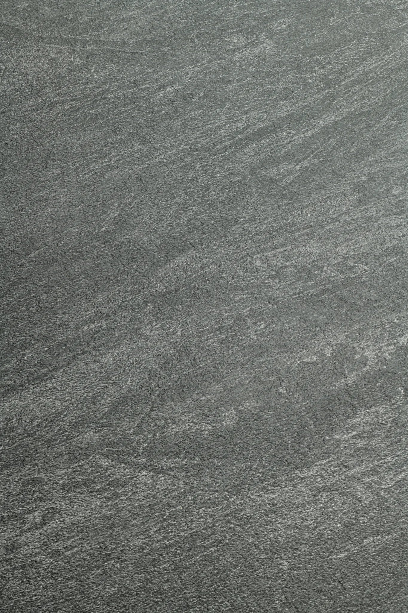 A close-up of a dark gray stone or concrete-like textured surface with subtle lighter gray veining and grain.