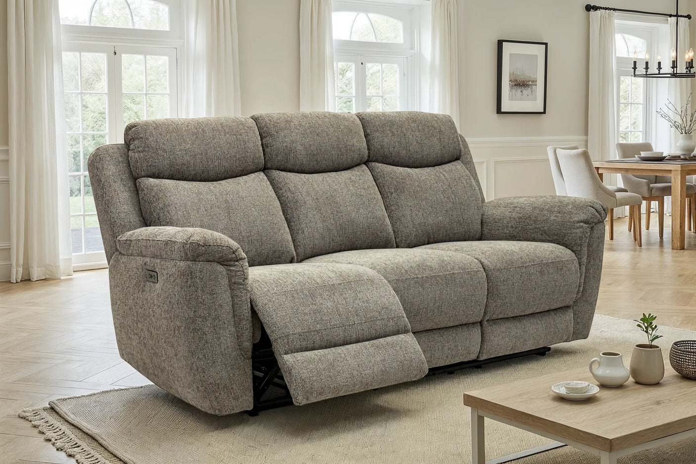 A three-seat power reclining loveseat sofa upholstered in textured gray fabric, shown in a bright, modern living room with one seat reclined.