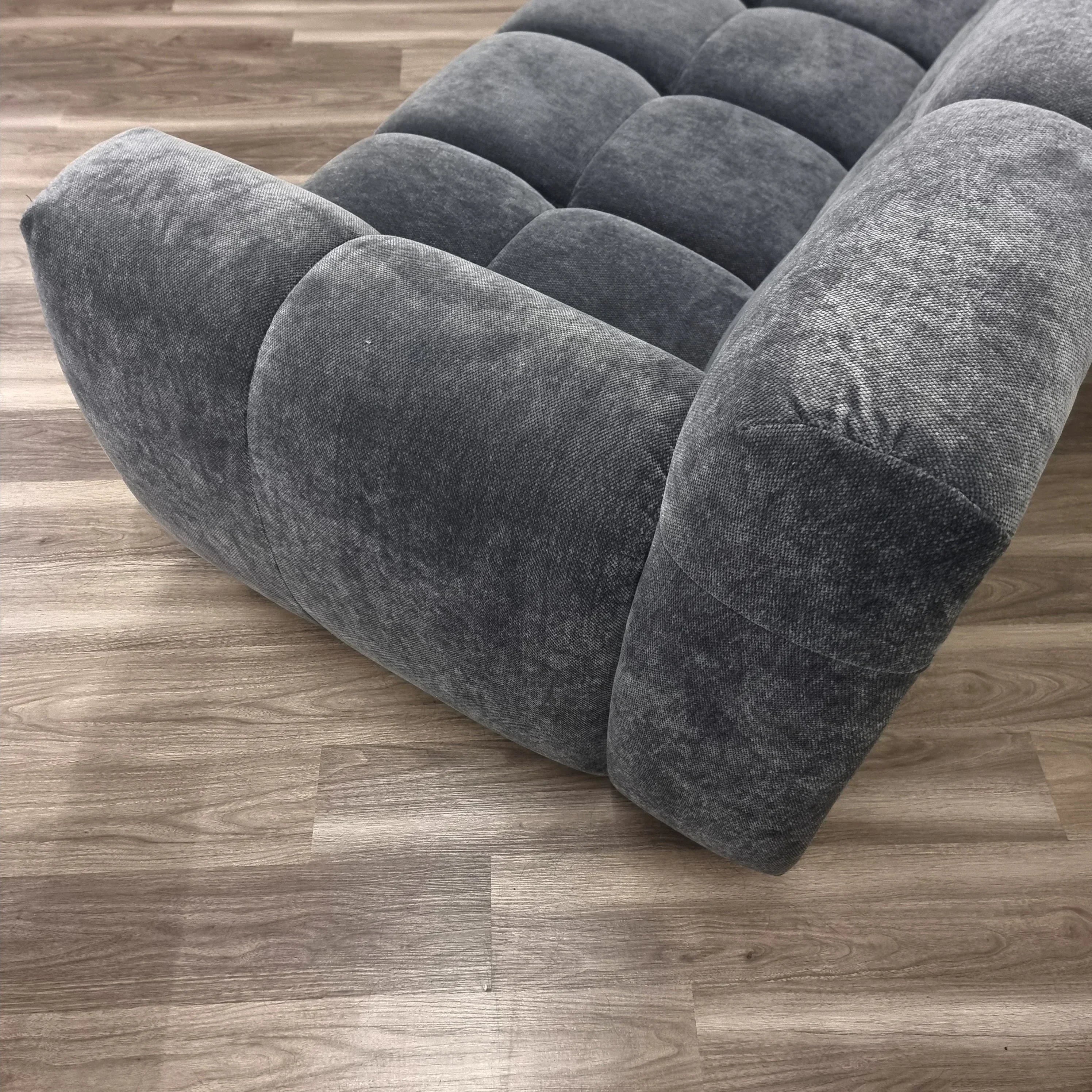 Grey corner sofa with tufted cushions and soft fabric on wooden floor