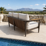 Beige cushioned sofa with dark brown metal frame beside a blue tiled pool and stone wall.