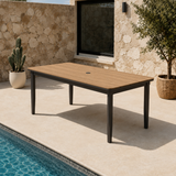 Light brown wooden tabletop with black metal legs beside pool and stone wall background