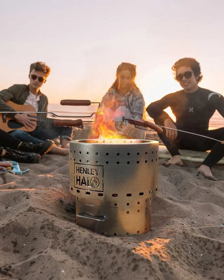 Stainless steel fire pit on the beach with people cooking marshmallows at sunset