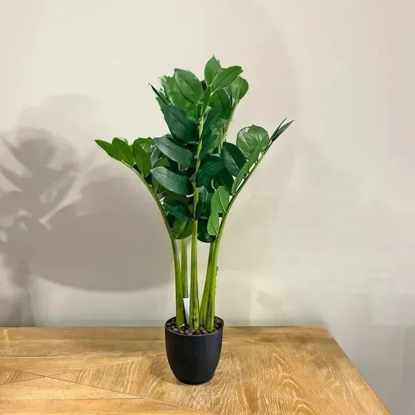 Artificial potted house plant with green leaves on a wooden table