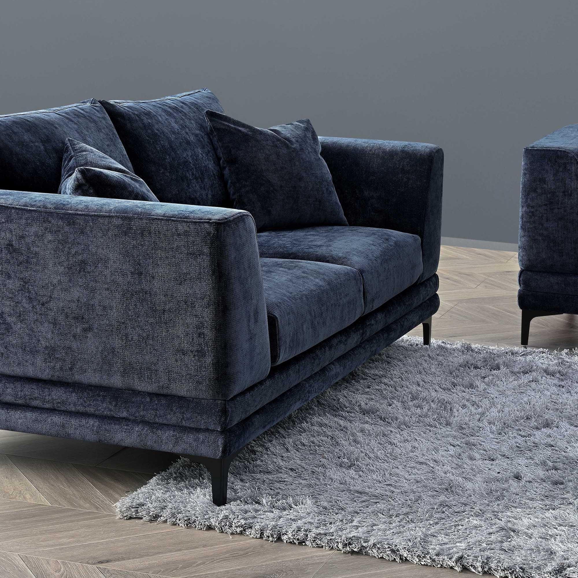 Blue velvet sofa with plush cushions and black legs on a grey rug and wooden floor