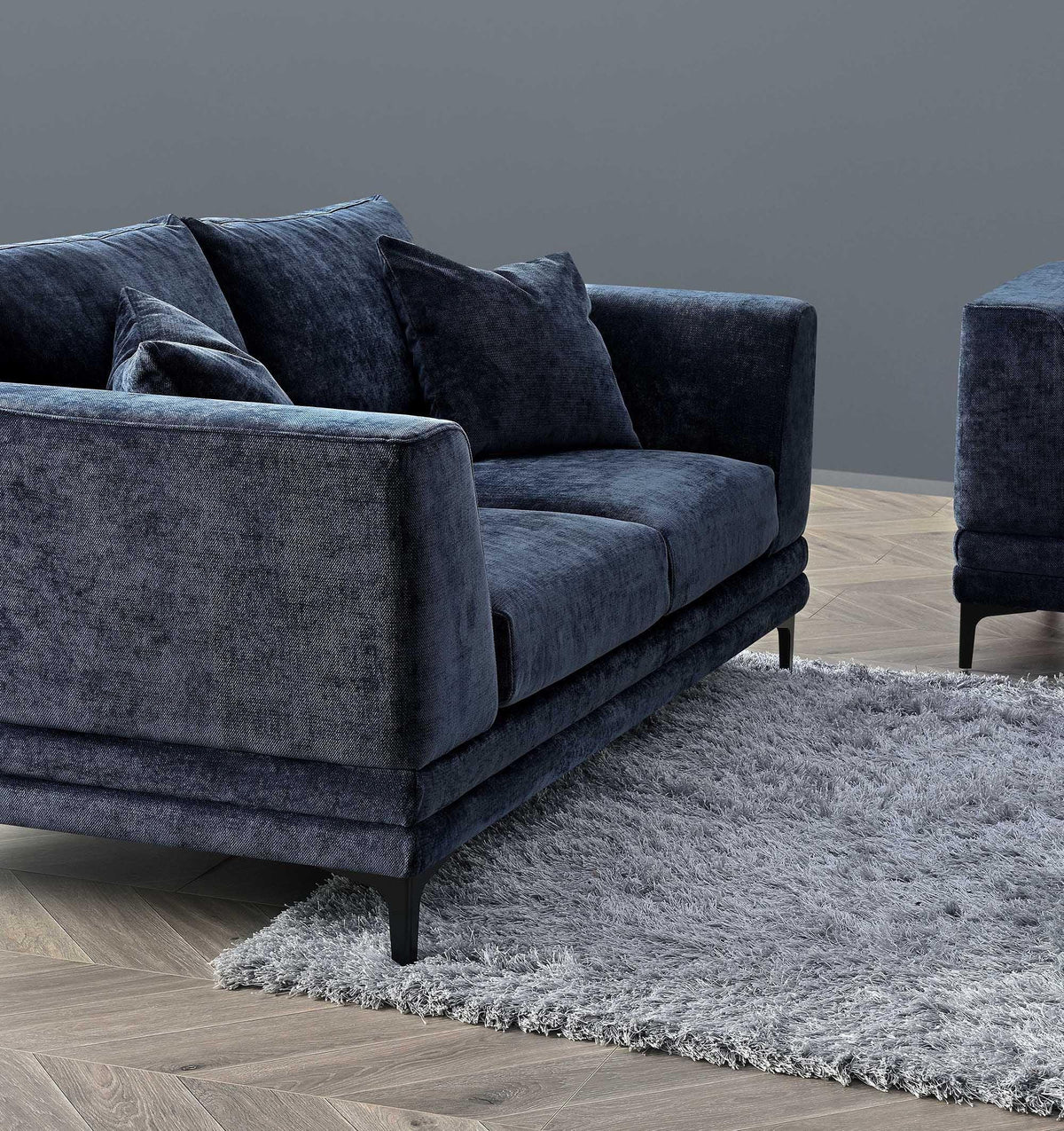Blue velvet sofa with plush cushions and black legs on a grey rug and wooden floor