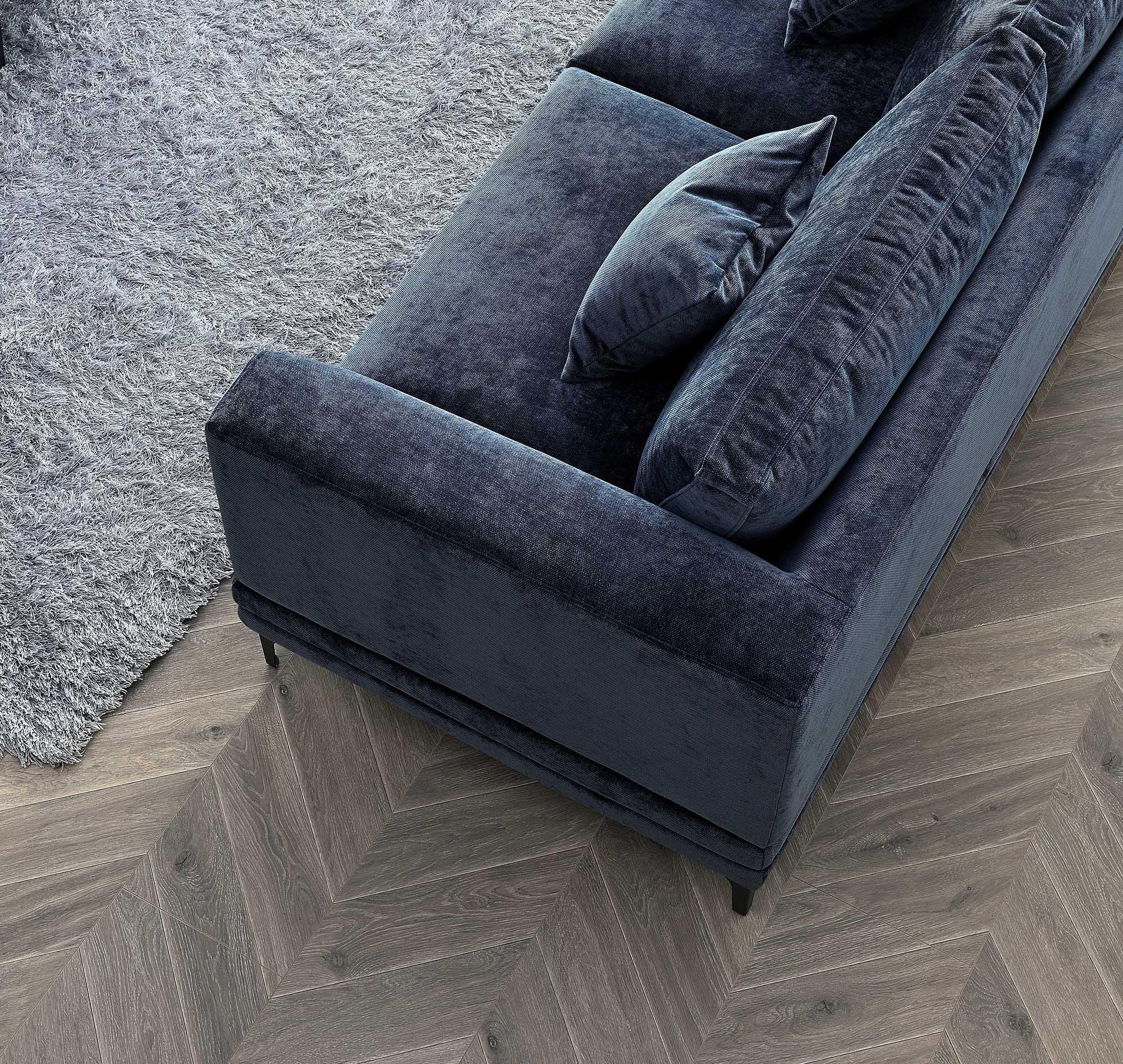 Blue velvet sofa with matching cushions on herringbone wood floor next to grey rug