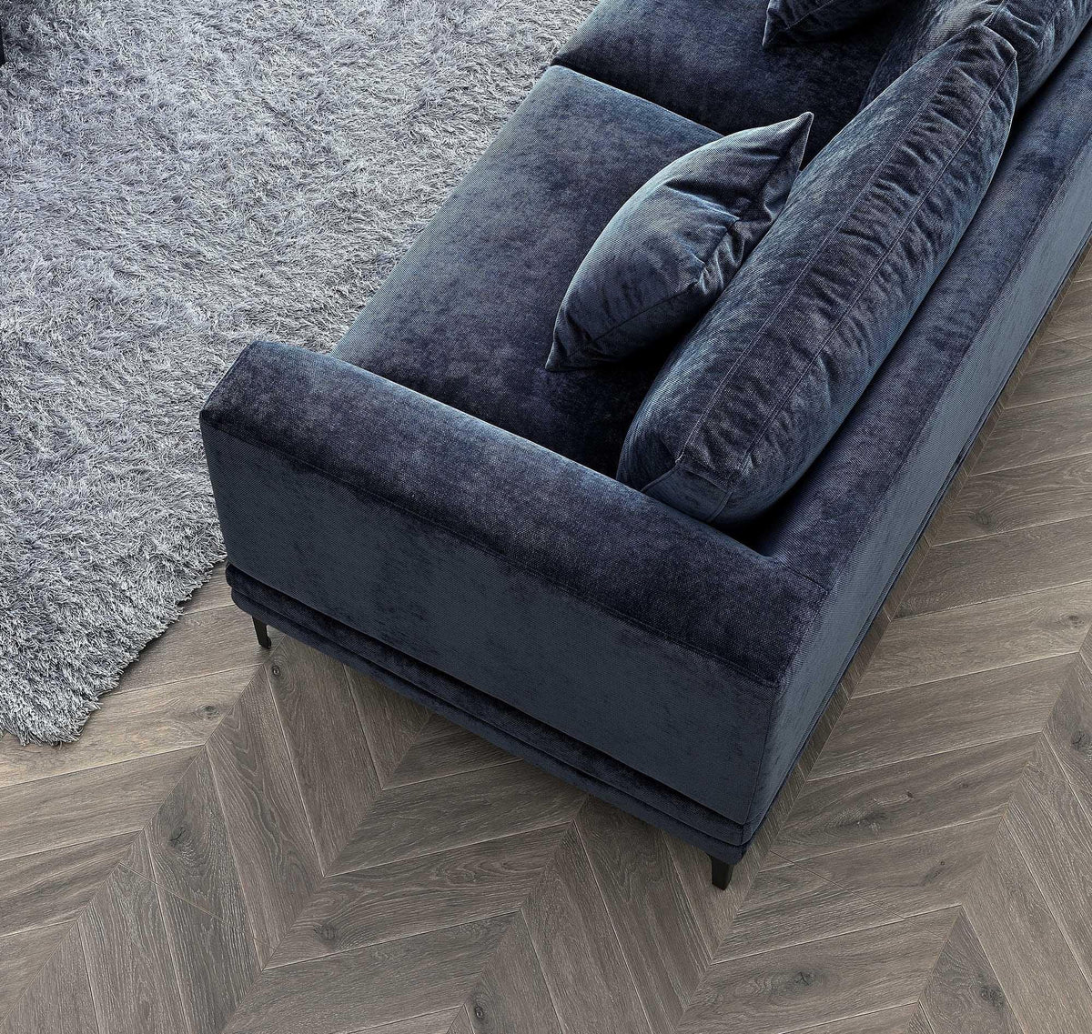 Blue velvet sofa with matching cushions on herringbone wood floor next to grey rug