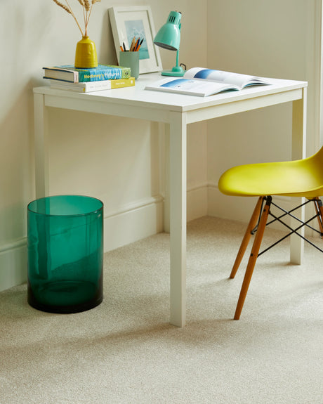 White desk with open book and green lamp in a cozy study corner with beige carpet.