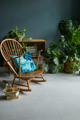 Wooden rocking chair with blue patterned cushion in a room with plants and books.