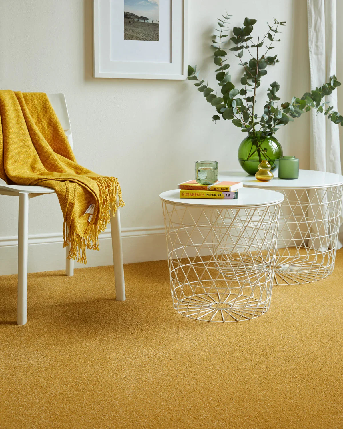Mustard yellow carpet in living room with white chair and round wire tables