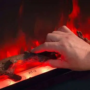 A hand adjusting the logs in an Atmos electric fire, showcasing realistic flames and glowing embers.