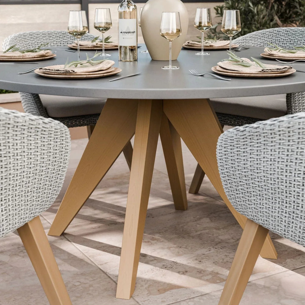 Round grey outdoor dining table with wooden legs and rattan chairs set for four