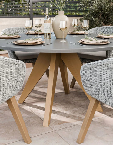 Round grey outdoor dining table with wooden legs and rattan chairs set for four