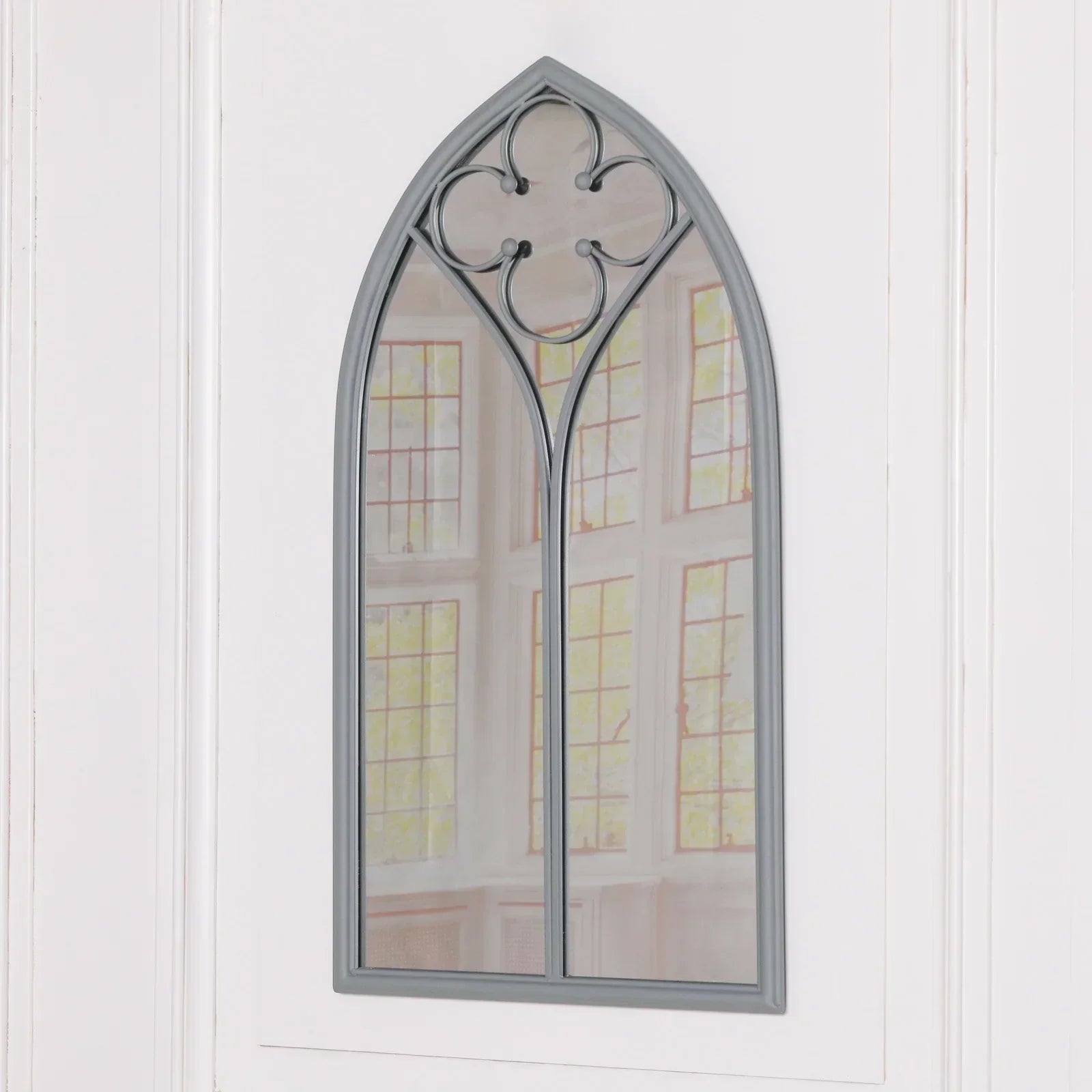 arched wall mirror with grey metal frame and quatrefoil detail mounted on white panel wall