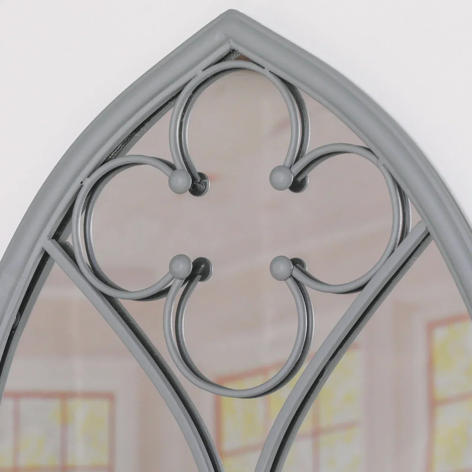 Close up of arched wall mirror with grey metal frame and decorative scrollwork detail