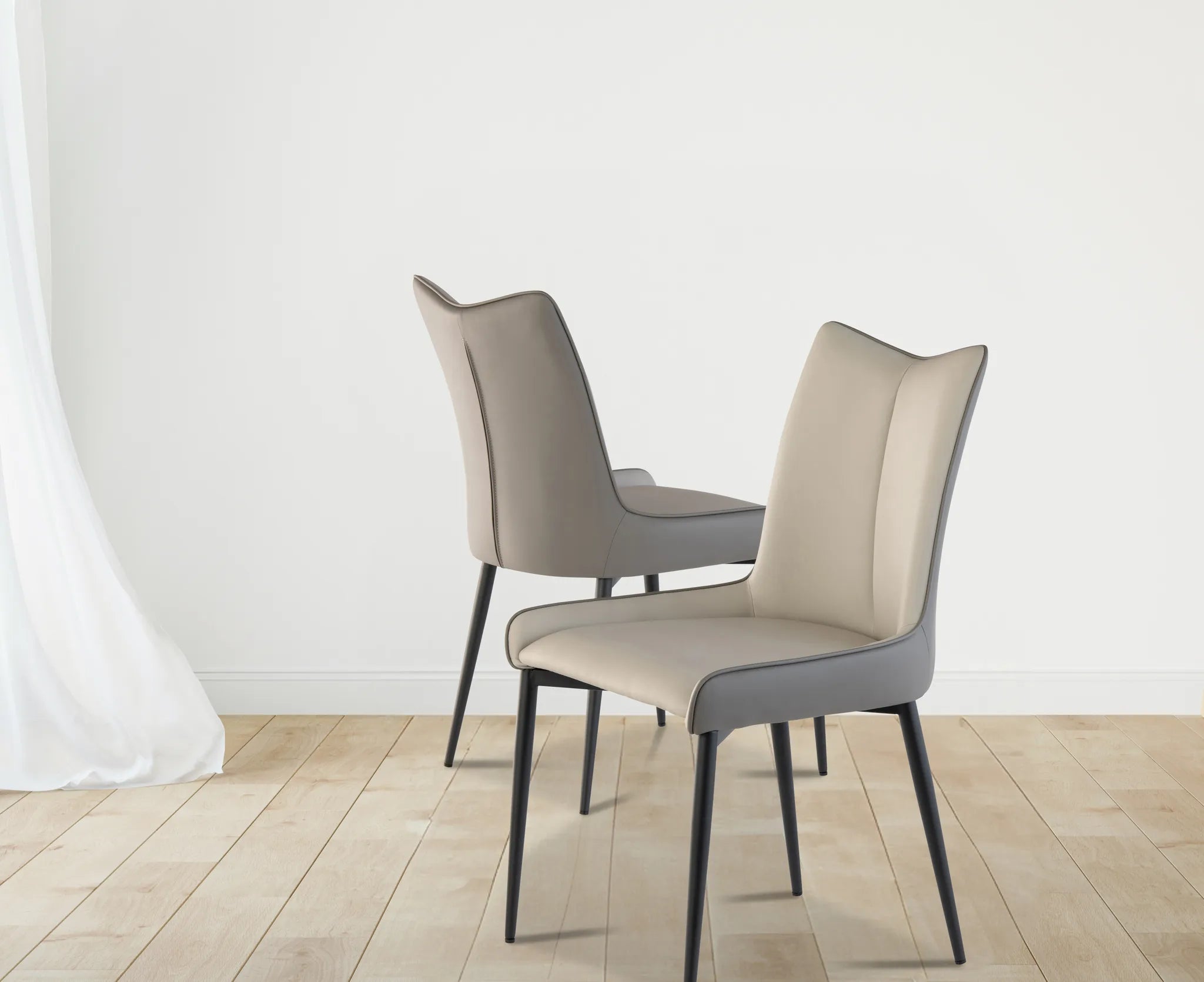 Two modern dining chairs with light beige and gray upholstered seats and backs, supported by slim black metal legs, set against a minimalist white wall and light wood floor.