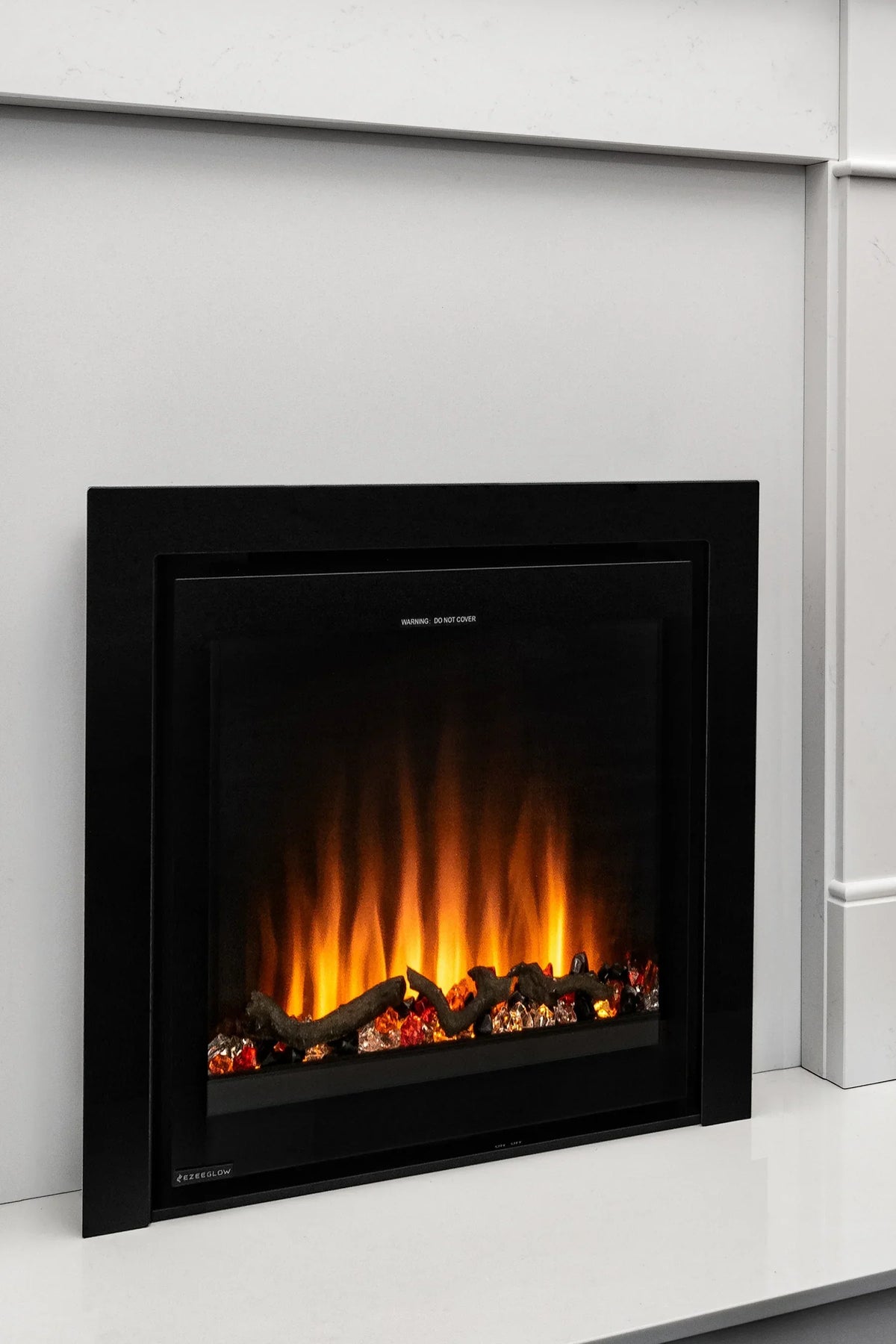 Modern electric fireplace insert with black frame in white surround, flames and log effect