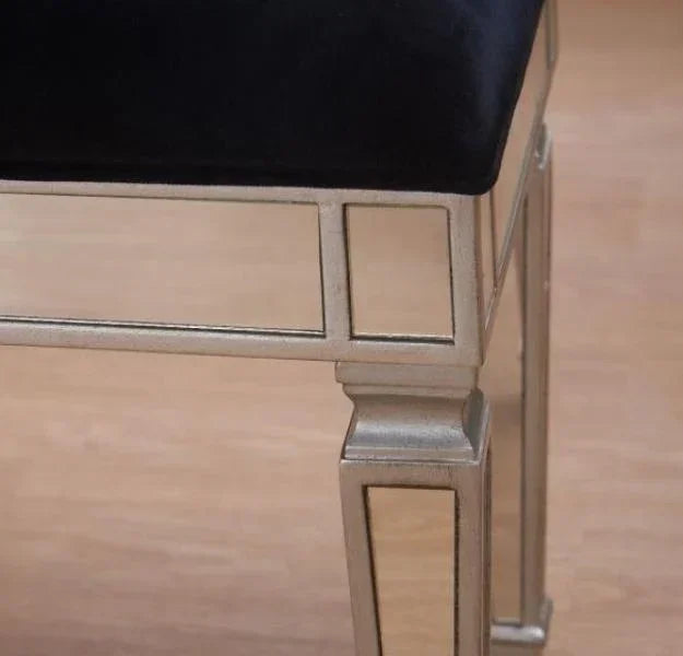 Mirrored dressing table stool with silver legs and black velvet seat on wooden floor