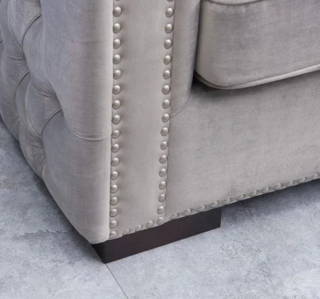 Close-up of grey velvet sofa with button-tufted back and silver stud detailing