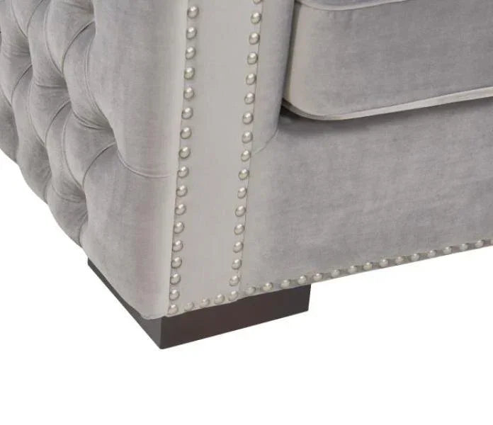 Grey velvet sofa armrest with button tufting and silver stud detailing on wooden feet
