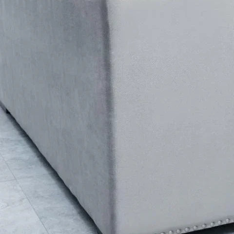 Closeup of light grey fabric sofa corner with stud detailing and dark wooden leg