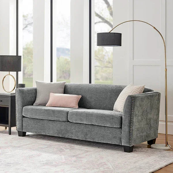 Grey fabric sofa with nailhead trim and scatter cushions in bright living room