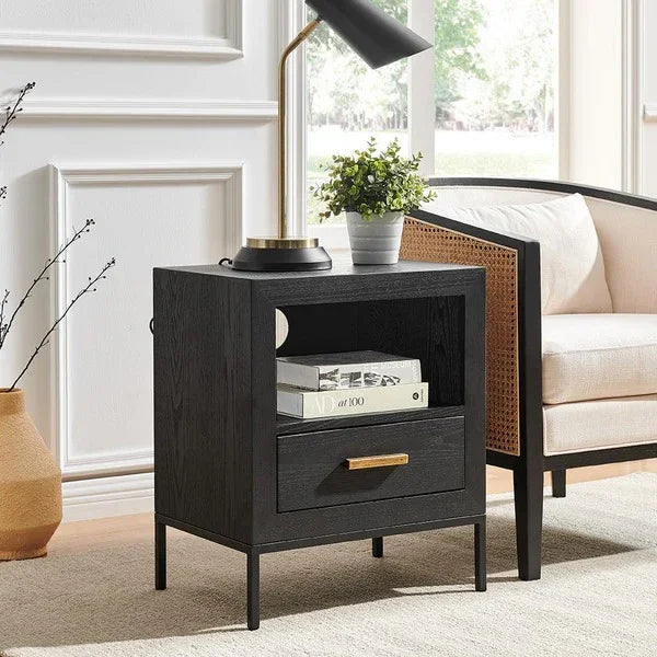 Black wood bedside table with open shelf and drawer beside cream armchair
