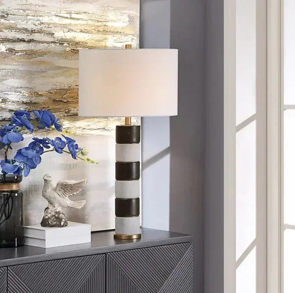 Striped ceramic table lamp with white shade on sideboard beside blue flowers and decor