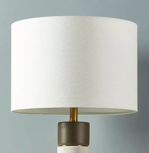 White drum lamp shade on a modern table lamp with muted blue background