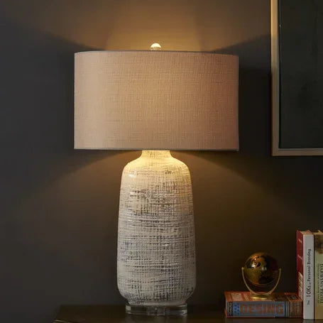 Ceramic table lamp with textured white base and beige fabric shade on sideboard